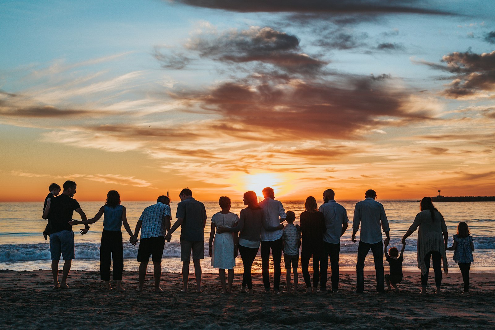Three generations of a family holding hands on the beach at sunset